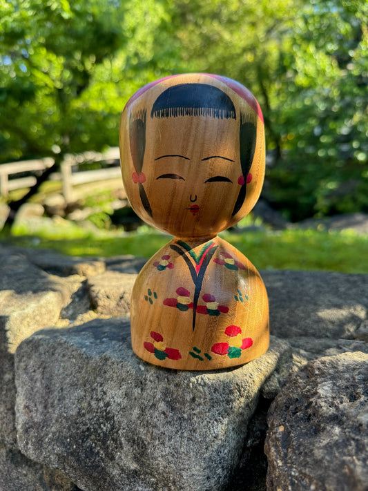 kokeshi poupée japonaise traditionnelle en bois, représentée en buste au visage souriant avec cheveux longs noués et kimono à fleur