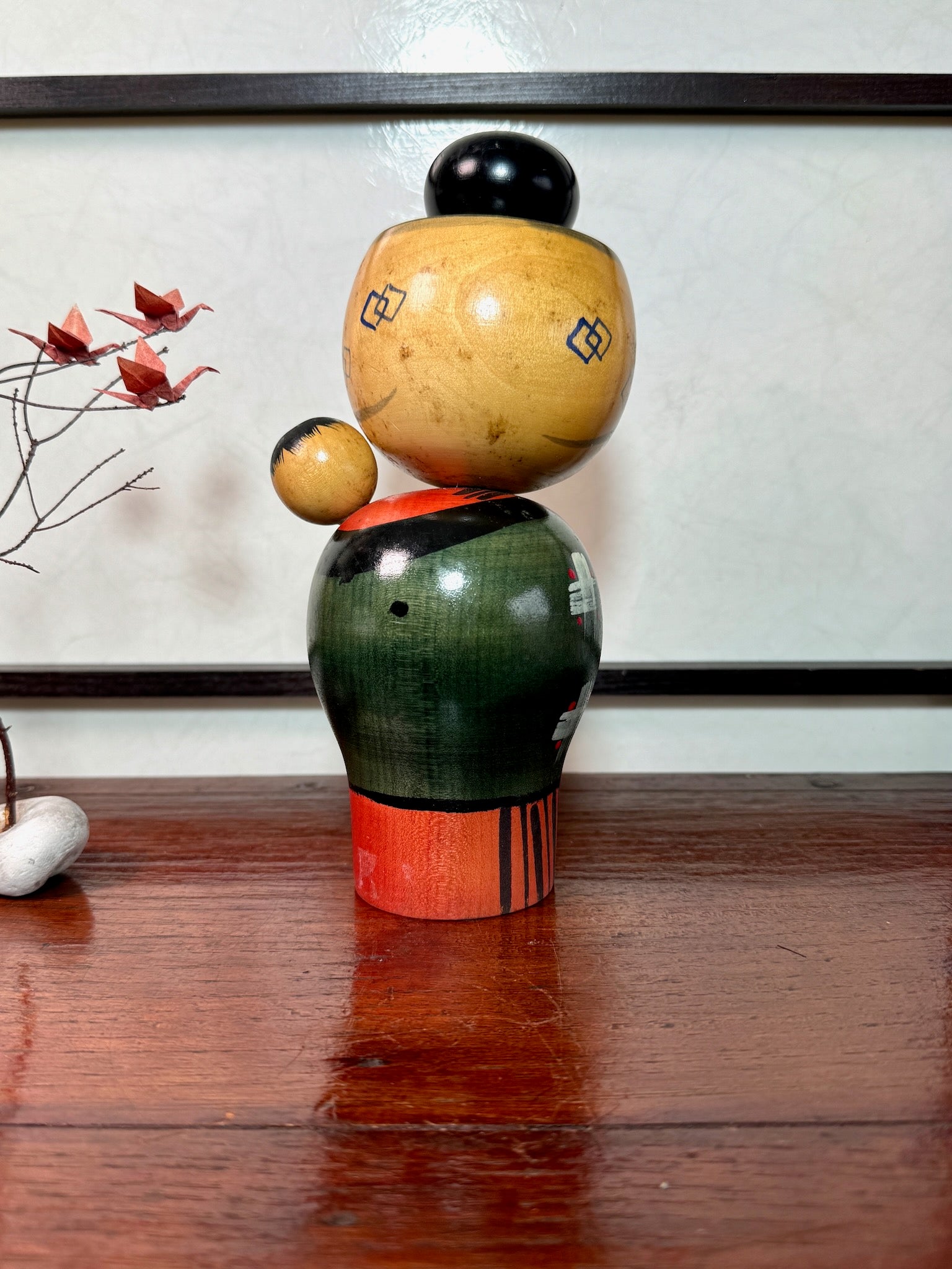 kokeshi babysitter de Miyashita Hajime, porte un enfant sur son dos, kimono vert et rouge, chignon sur la tête, vu de dos