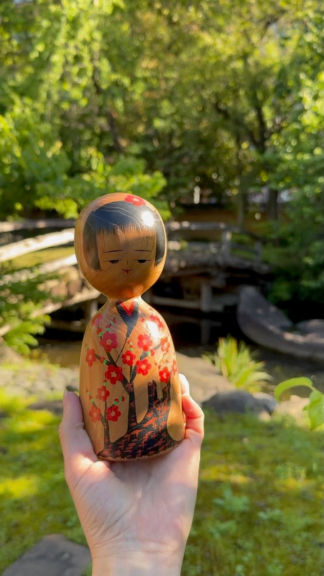 kokeshi, poupée japonaise traditionnelle en bois avec un motif de cerisier en fleurs, tenue dans une main