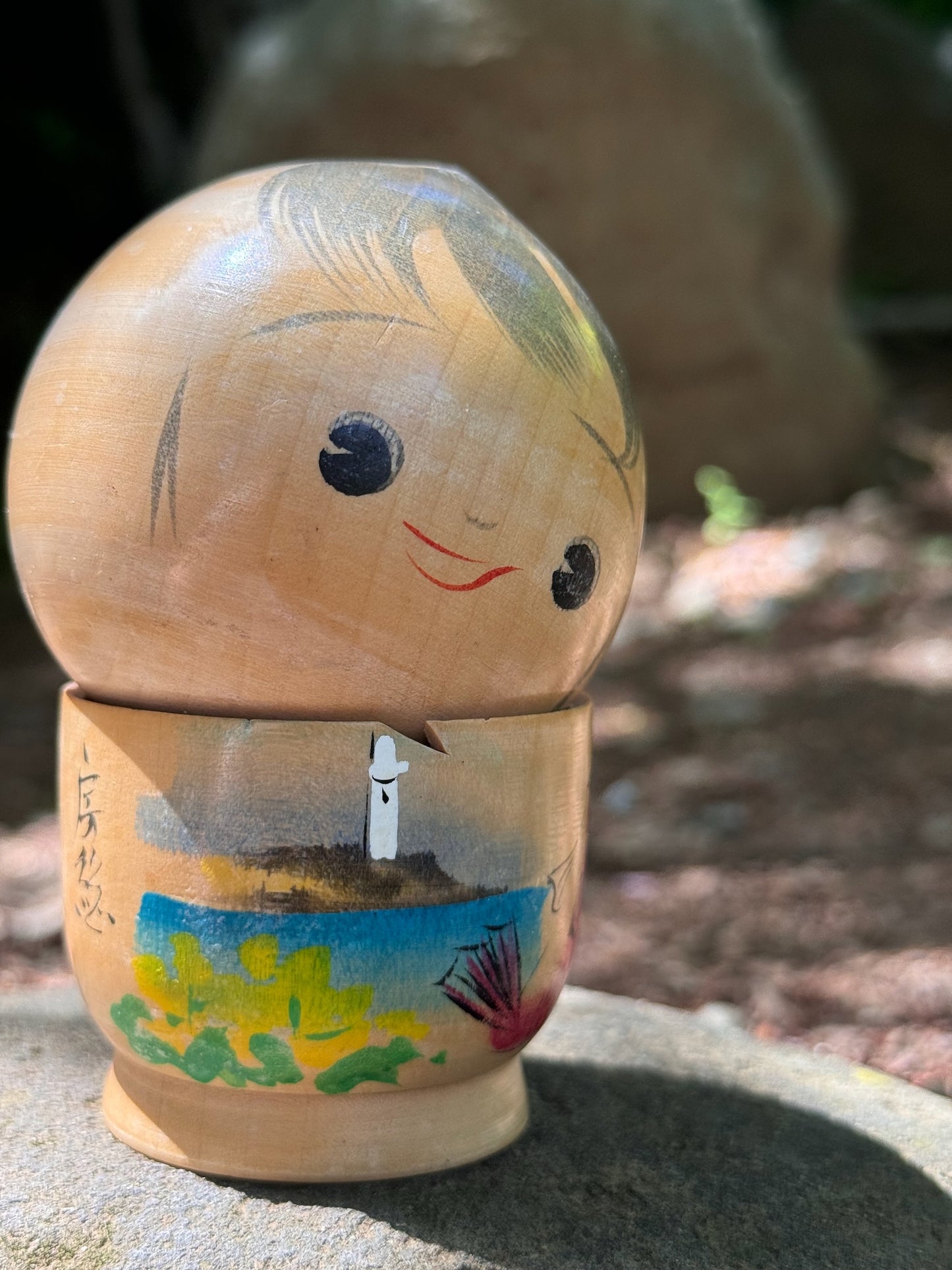 kokeshi poupée japonaise en bois souriante avec paysage bord de mer et poisson, gros plan