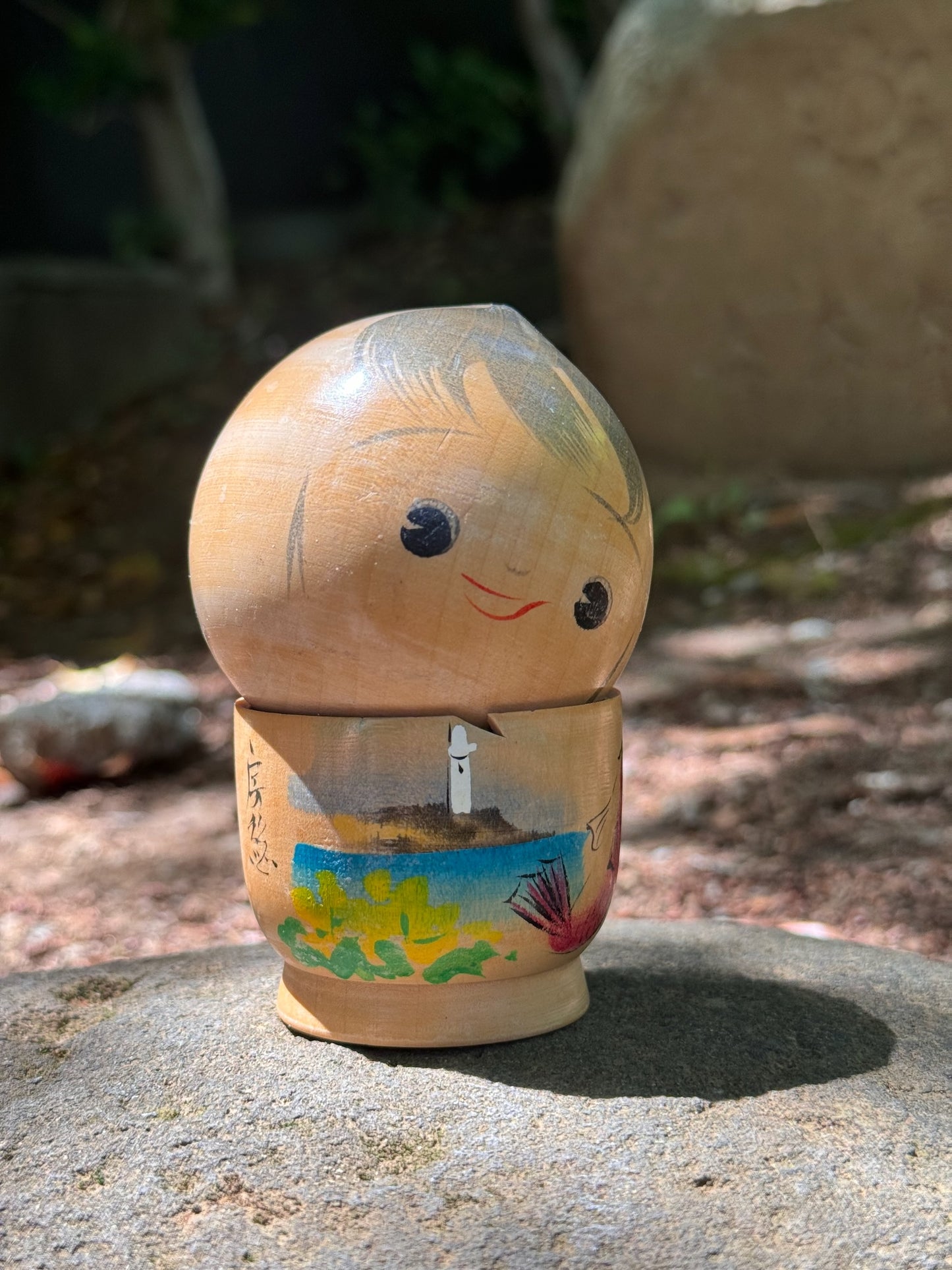 kokeshi poupée japonaise en bois souriante avec paysage bord de mer et poisson, vu de 3/4