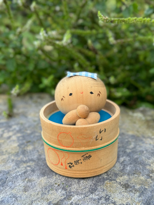 Kokeshi souvenir du Onsen de Kinosaki, poupée japonaise en bois dans son bain, tête ronde petits yeux rieurs, serviette sur sa tête dans bain en bois rond. 