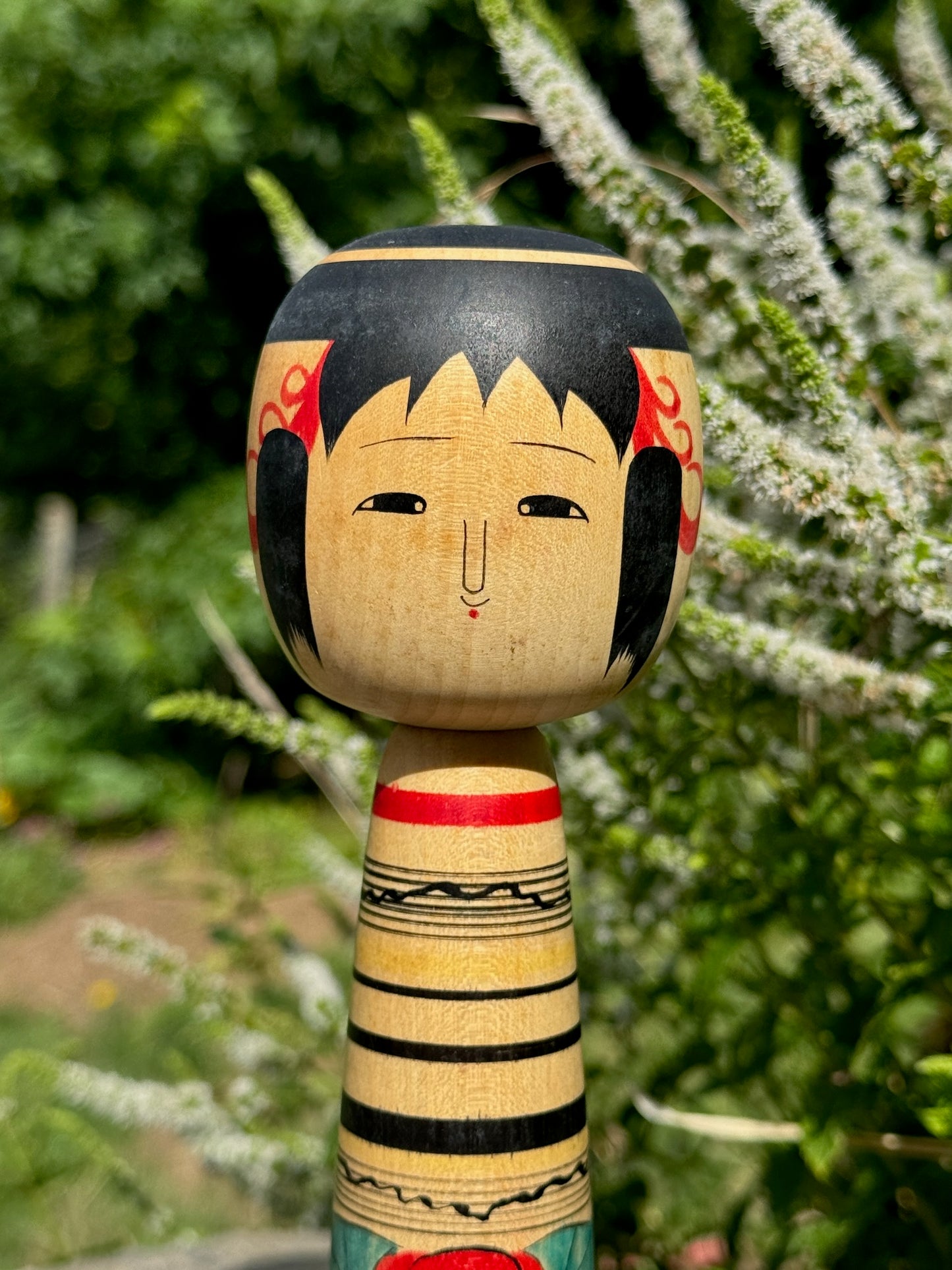 kokeshi, poupée japonaise traditionnelle en bois de Abe Kazue, à rayures et motif pivoine rouge, gros plan sur le visage souriant