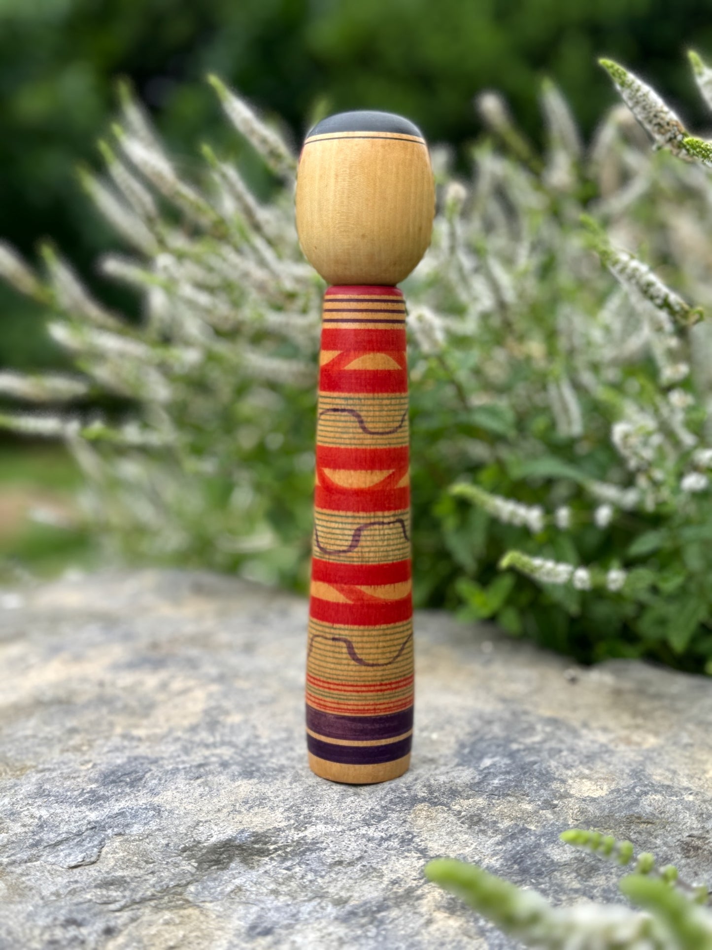 Kokeshi traditionnelle, poupée en bois japonaise de l'artisan Saito Hiromichi,  style Tsuchiyu. Visage souriant, corps long avec vague rouges rokuro et ondulations violettes.  Dos de la Kokeshi.