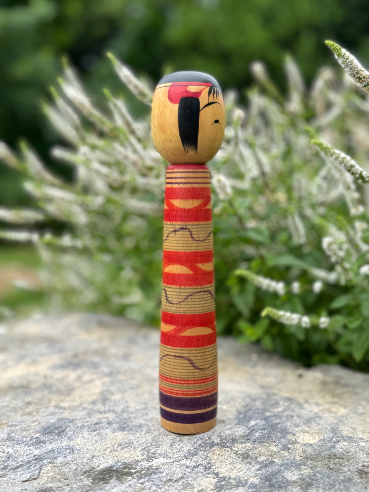 Kokeshi traditionnelle, poupée en bois japonaise de l'artisan Saito Hiromichi,  style Tsuchiyu. Visage souriant, corps long avec vague rouges rokuro et ondulations violettes. profil mèche de cheveux. 
