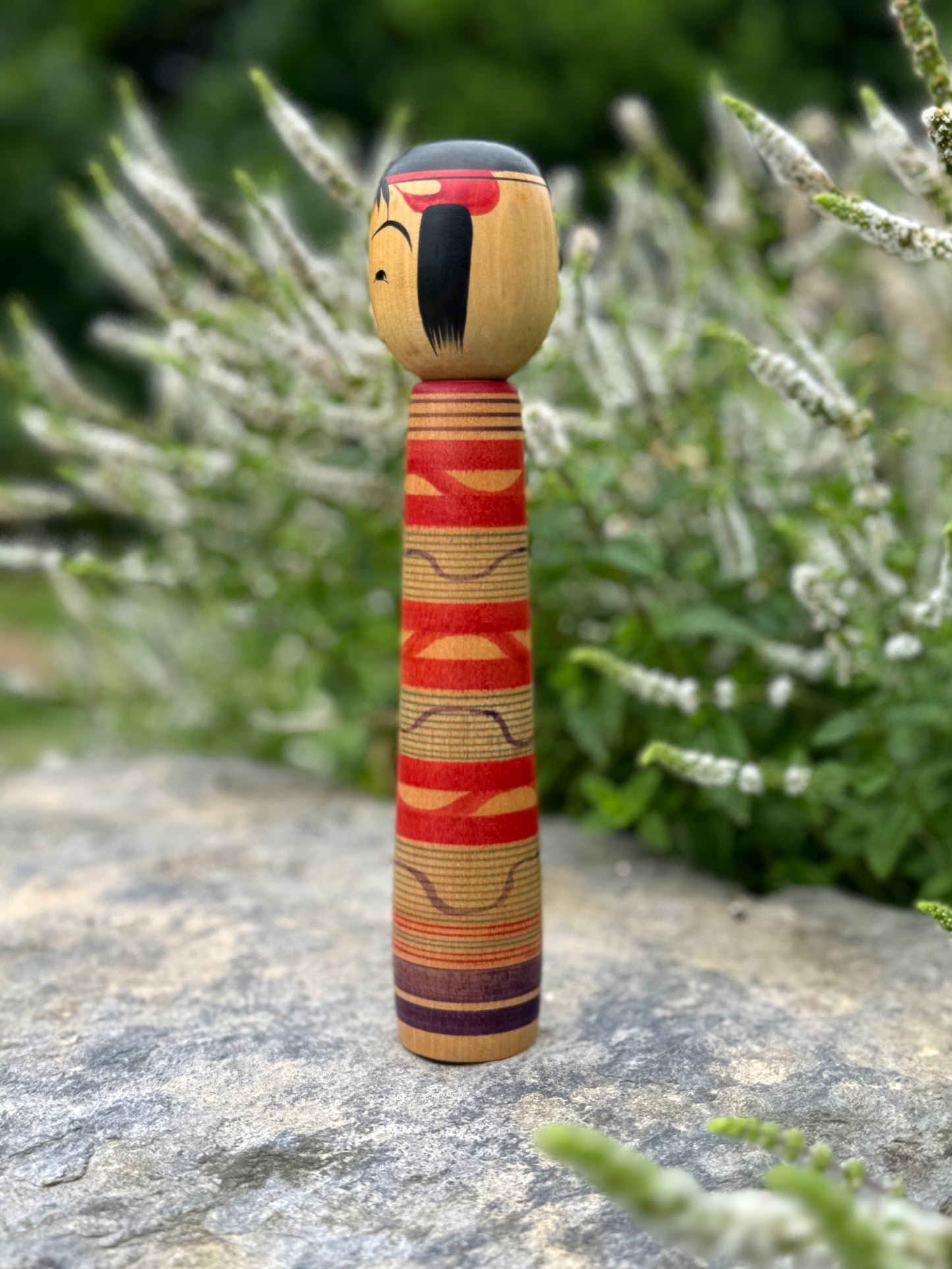 Kokeshi traditionnelle, poupée en bois japonaise de l'artisan Saito Hiromichi,  style Tsuchiyu. Visage souriant, corps long avec vague rouges rokuro et ondulations violettes. Profil cheveux et ondulations.