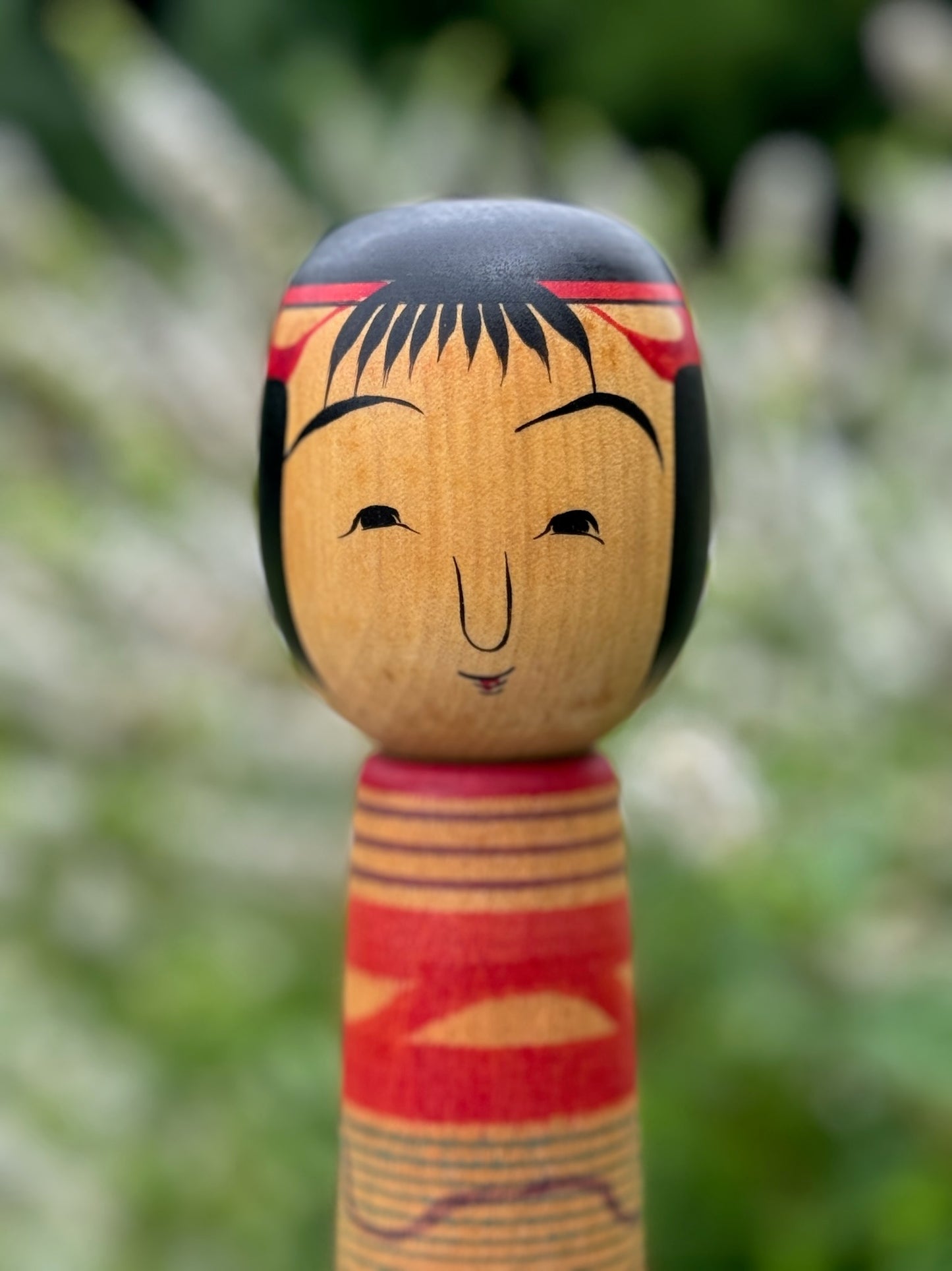 Kokeshi traditionnelle, poupée en bois japonaise de l'artisan Saito Hiromichi,  style Tsuchiyu. Visage souriant, nez proéminent, yeux joyeux et bouche souriante. Cheveux en frange noire et rouge.  