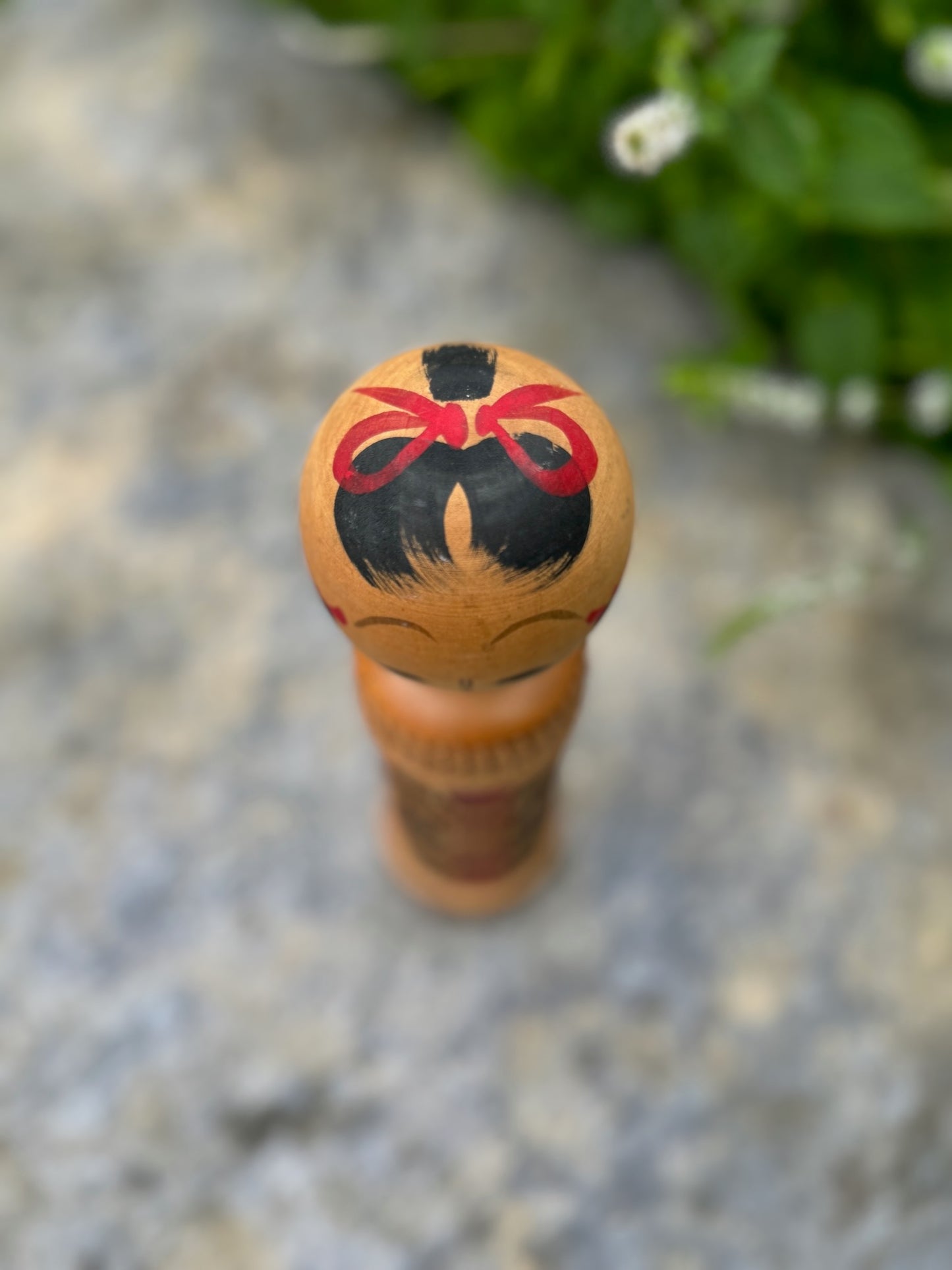 kokeshi, poupée japonaise en bois au corps en tatami à motif géométrique rouge et noir, vu de dessus noeud rouge peint sur cheveux noir