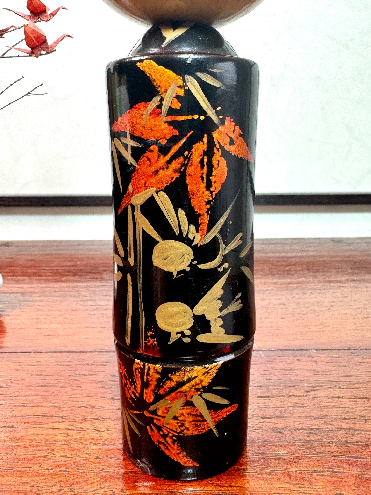 kokeshi, poupée japonaise en bois laqué noir de Takahashi Tatsuro, motif feuilles d'érable orange et bambou, gros plan sur les feuilles d'érables or et orangé