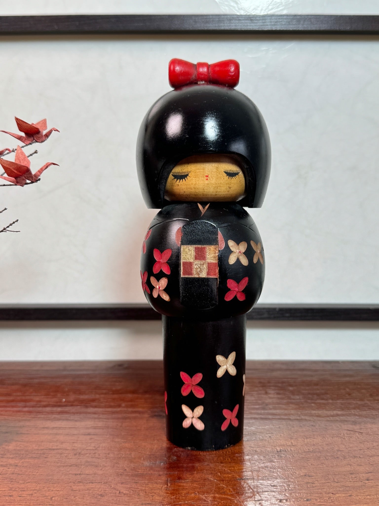 kokeshi de Miyashita Hajime, noire avec fleurs cerisier blanches et rouge, noeud rouge sur la tête