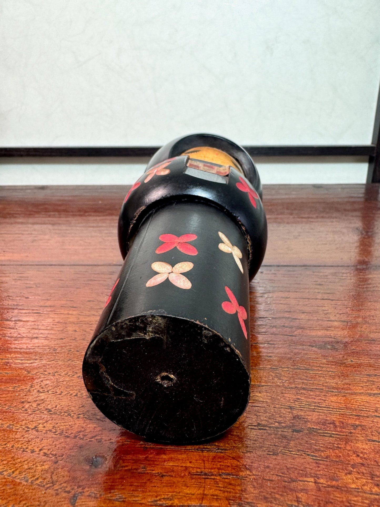 kokeshi de Miyashita Hajime, noire avec fleurs cerisier blanches et rouge, noeud rouge sur la tête, vu de dessous