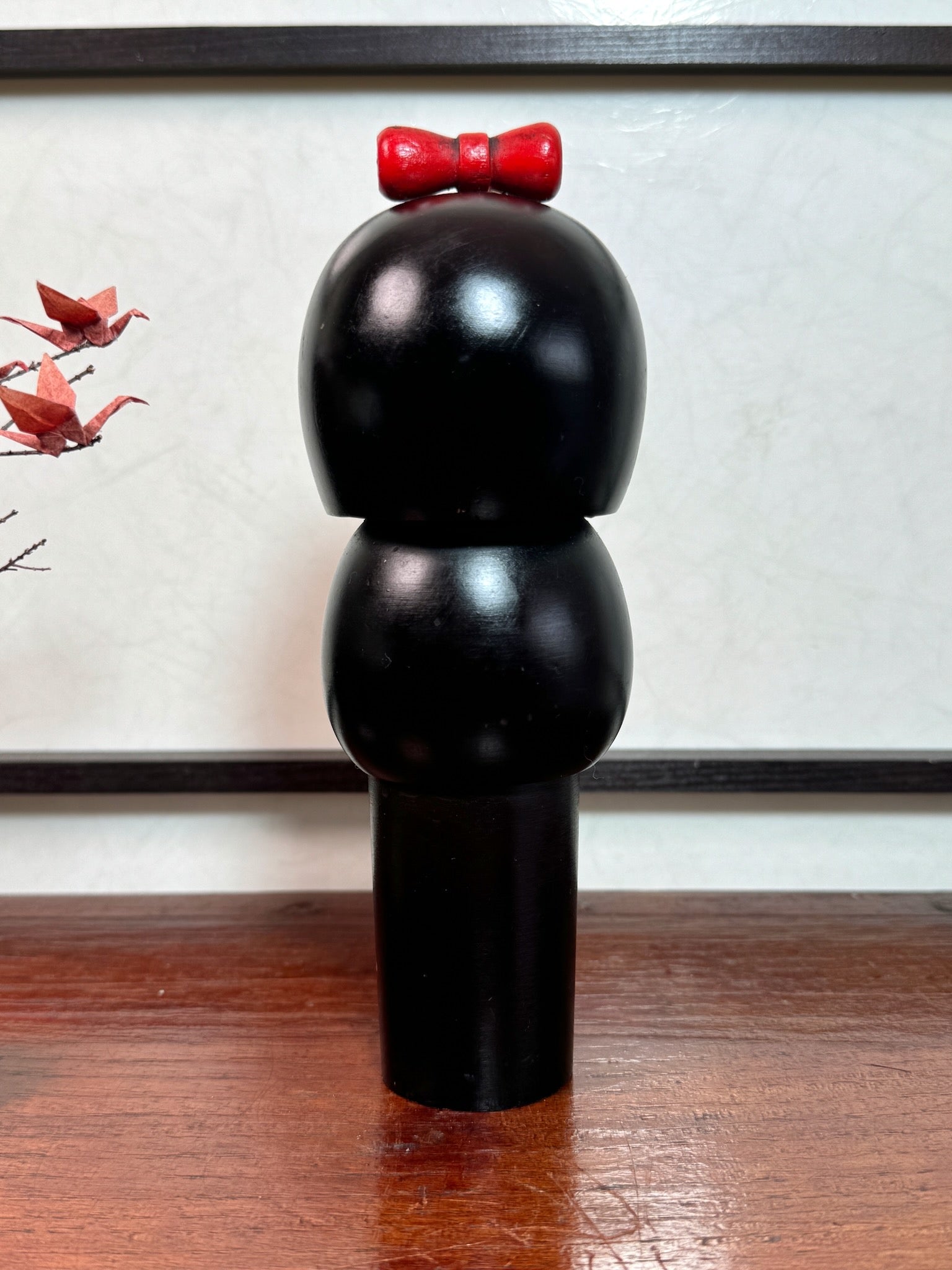 kokeshi de Miyashita Hajime, noire avec fleurs cerisier blanches et rouge, noeud rouge sur la tête, vu de dos