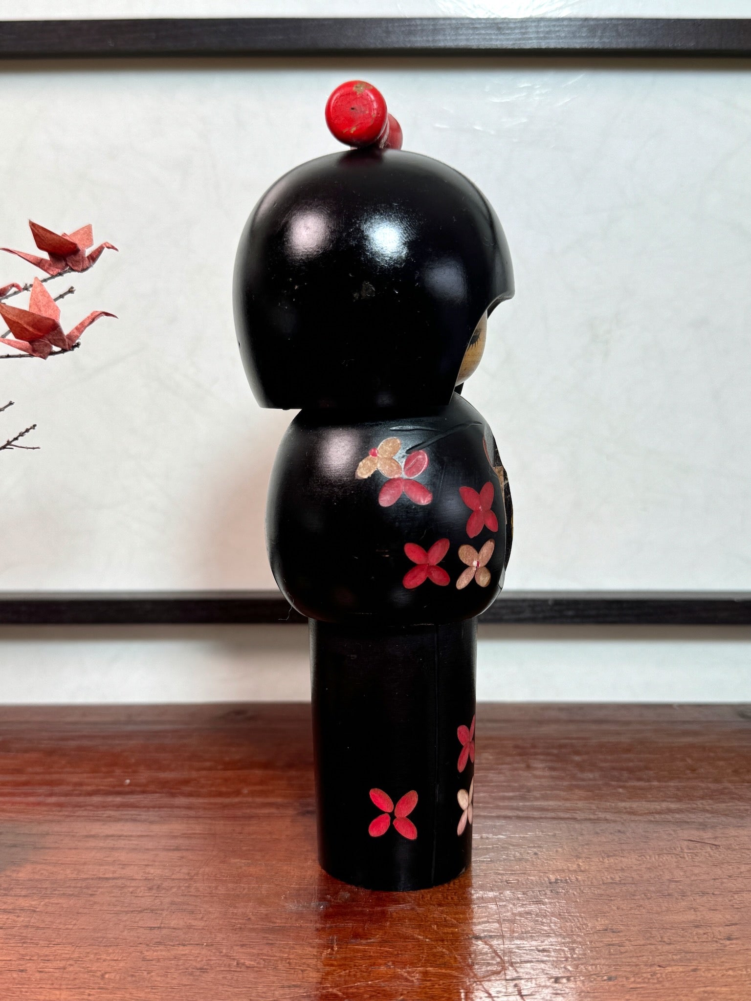 kokeshi de Miyashita Hajime, noire avec fleurs cerisier blanches et rouge, noeud rouge sur la tête, profil droit