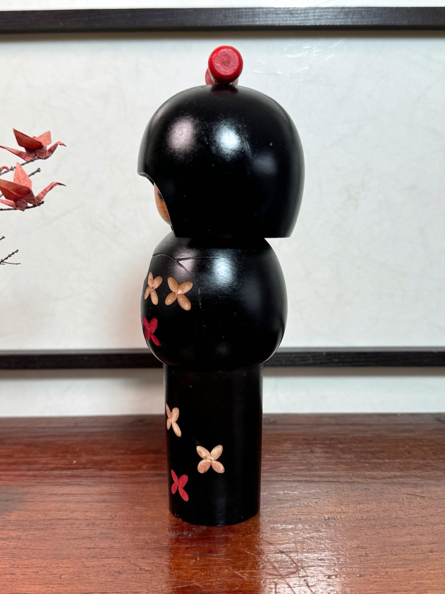 kokeshi de Miyashita Hajime, noire avec fleurs cerisier blanches et rouge, noeud rouge sur la tête, profil gauche