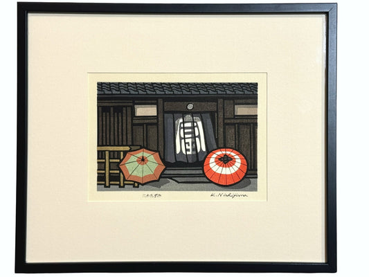 estampe japonaise contemporaine encadrée de Nishijima, deux parapluies bicolores séchant au soleil devant entree de maison avec un noren, avec cadre fin noir