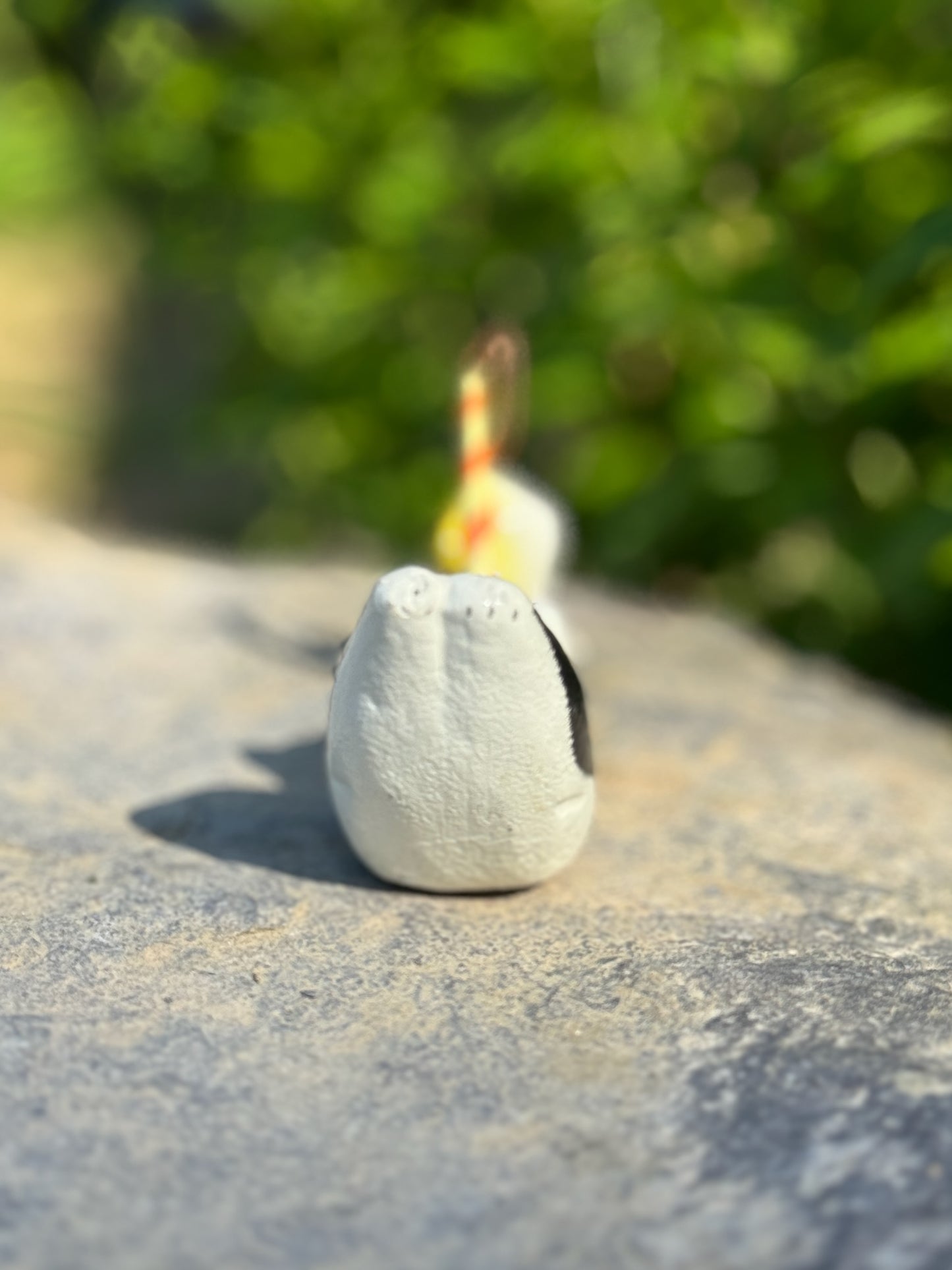 figurine japonaise, chat noir et blanc, allongé sur le ventre les pattes arriere en l'air, tenant une canne à pêche sur laquelle est suspendu un poisson, en papier maché, vu de dos