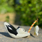 figurine japonaise, chat noir et blanc, allongé sur le ventre les pattes arriere en l'air, tenant une canne à pêche sur laquelle est suspendu un poisson, en papier maché