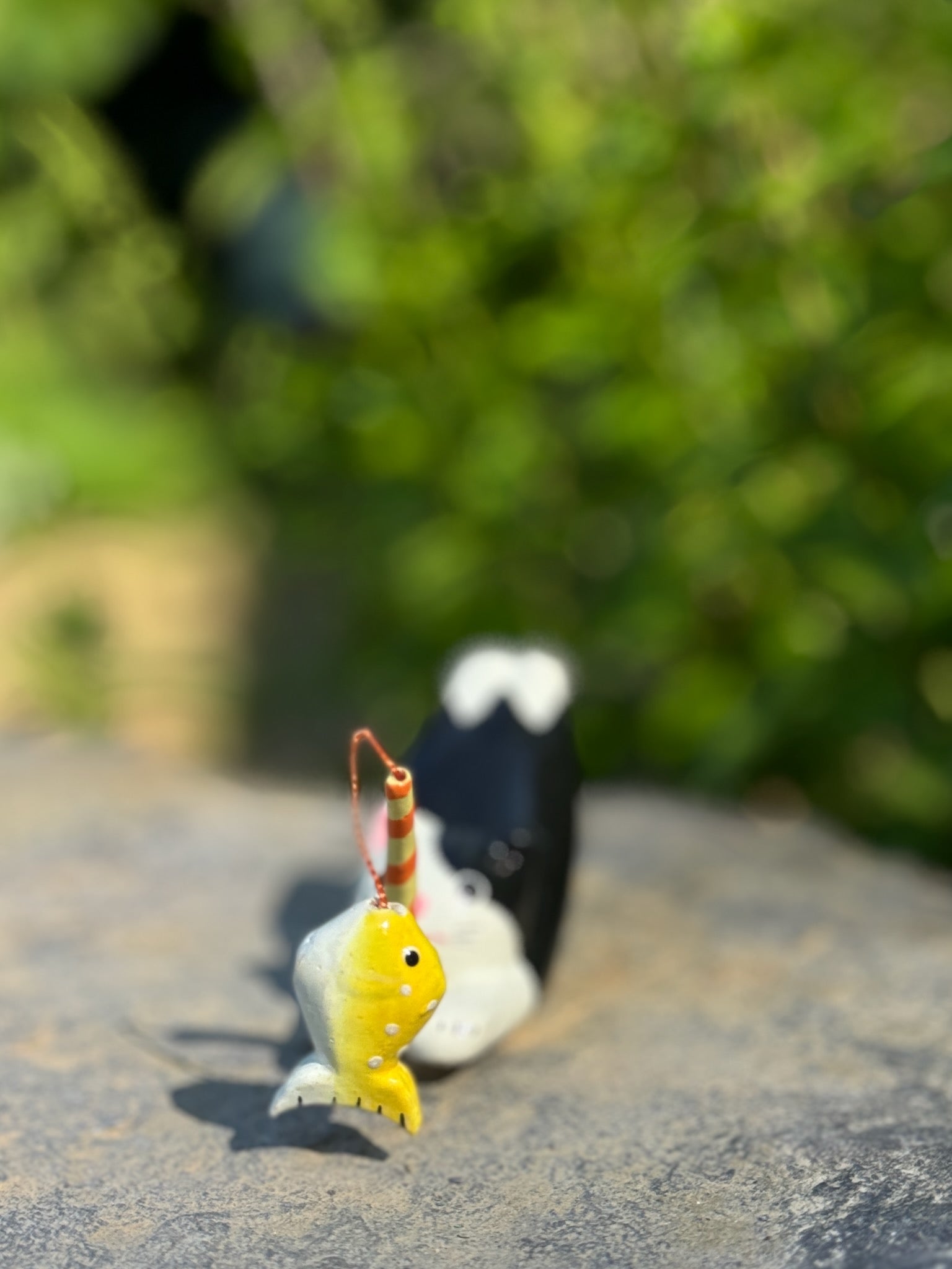 figurine japonaise, chat noir et blanc, allongé sur le ventre les pattes arriere en l'air, tenant une canne à pêche sur laquelle est suspendu un poisson, en papier maché, gros plan sur le poisson jaune