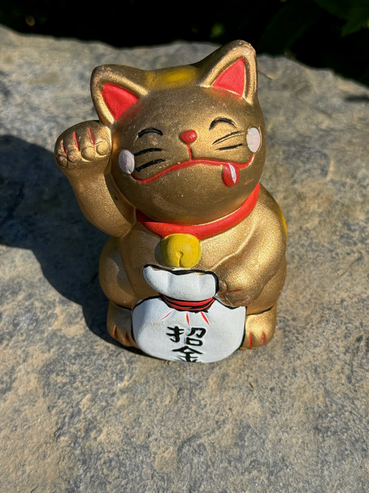 chat maneki-neko japonais en céramique or levant une patte, tenant un sac blanc avec inscription japonaise "invitation d'argent", en gros plan