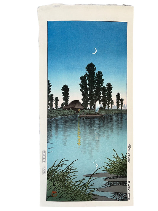 estampe japonaise d'un paysage nocturne de Hasui, avec un croissant de lune, une rivière, un bateaux à voile passant devant une chaumière éclairée