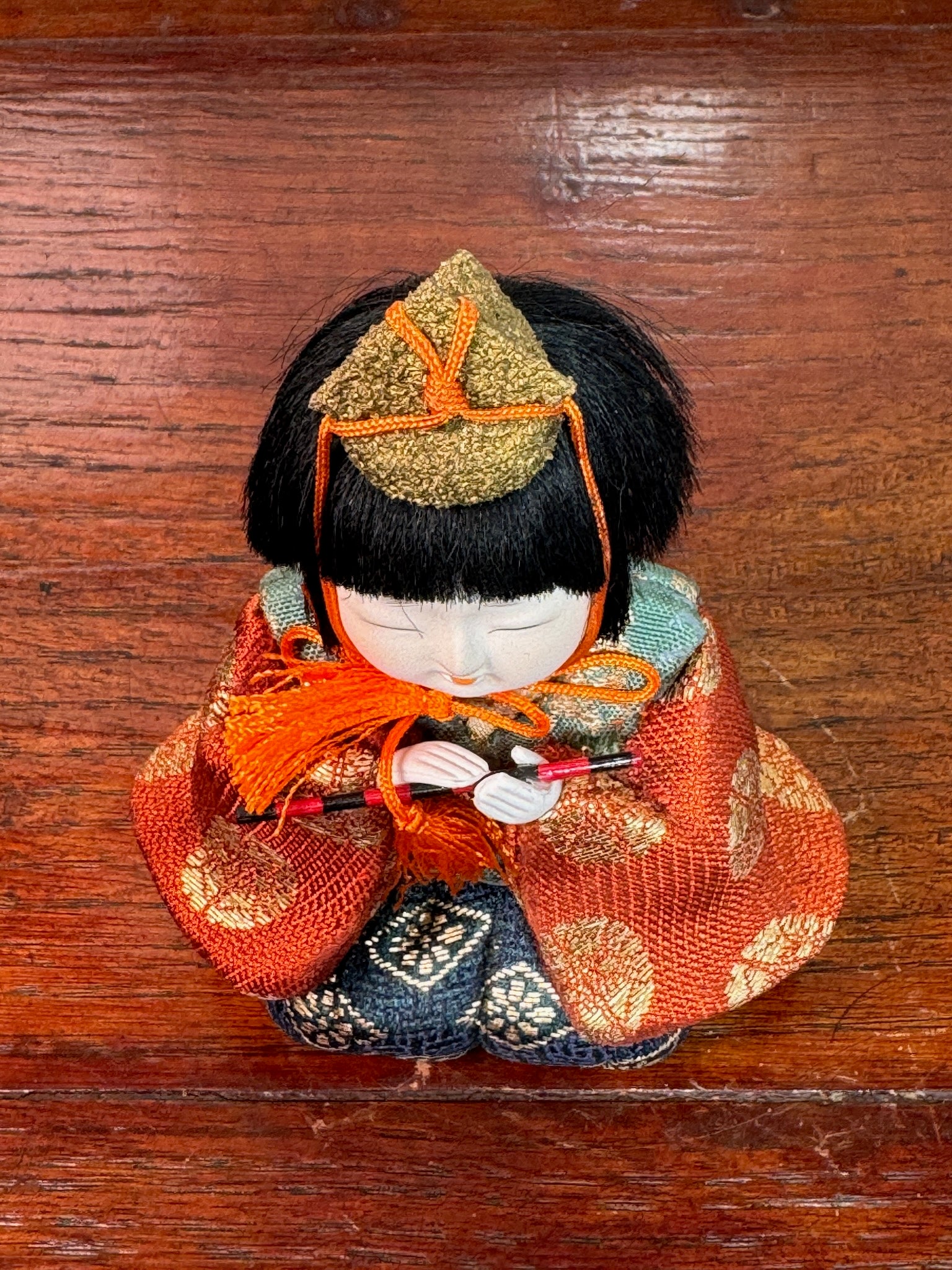 poupée japonaise gosho avec une flûte traversière dans les mains, en kimono orange. musicien pour le Hina Matsuri, vu de dessus chapeau doré