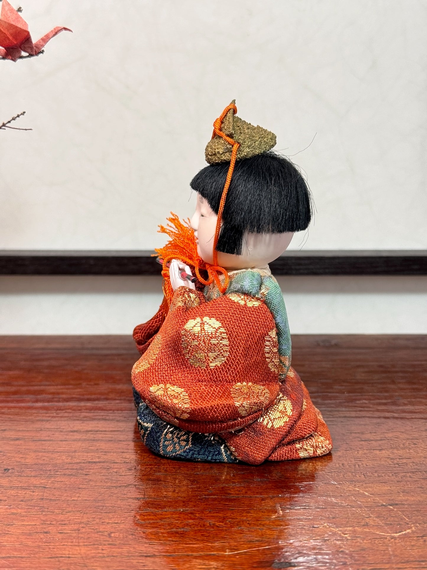 poupée japonaise gosho avec une flûte traversière dans les mains, en kimono orange. musicien pour le Hina Matsuri, profil gauche