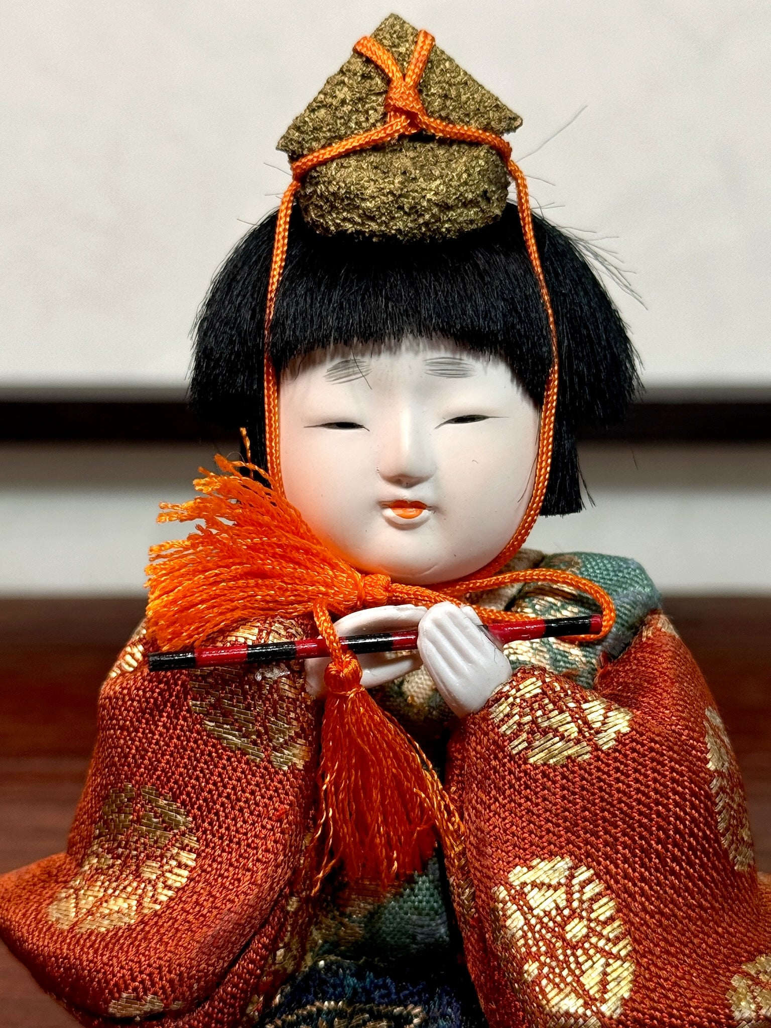 poupée japonaise gosho avec une flûte traversière dans les mains, en kimono orange. musicien pour le Hina Matsuri, gros plan sur le visage blanc et potelé