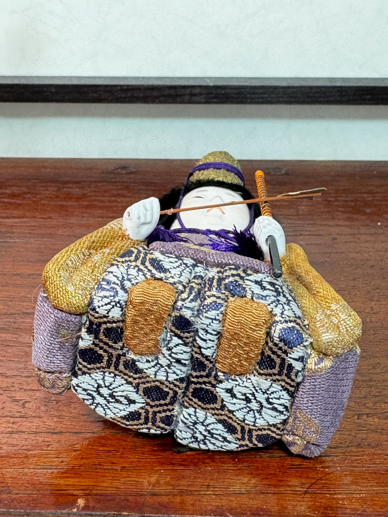 Poupée japonaise gosho kimekomi, un archer avec ses flèches dans le dos, une flèche dans une main vêtu d'un kimono violet et or, vu de dessous