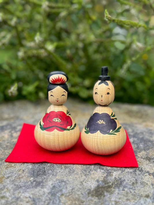 Couple de poupées kokeshi en bois avec motifs de pivoines rouges et bleues sur fond rouge




