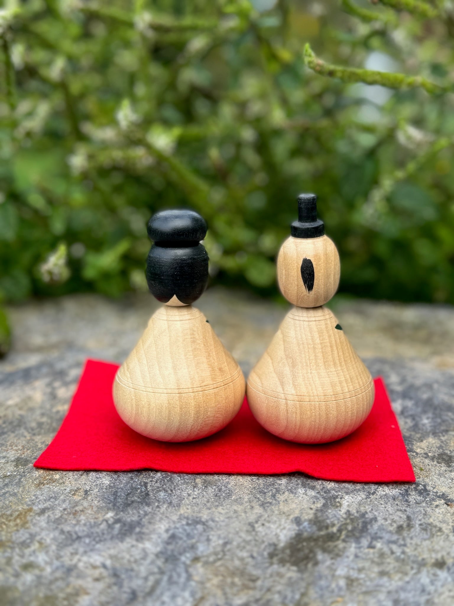 Couple de poupées kokeshi en bois avec motifs de pivoines rouges et bleues sur fond rouge vue derriere 