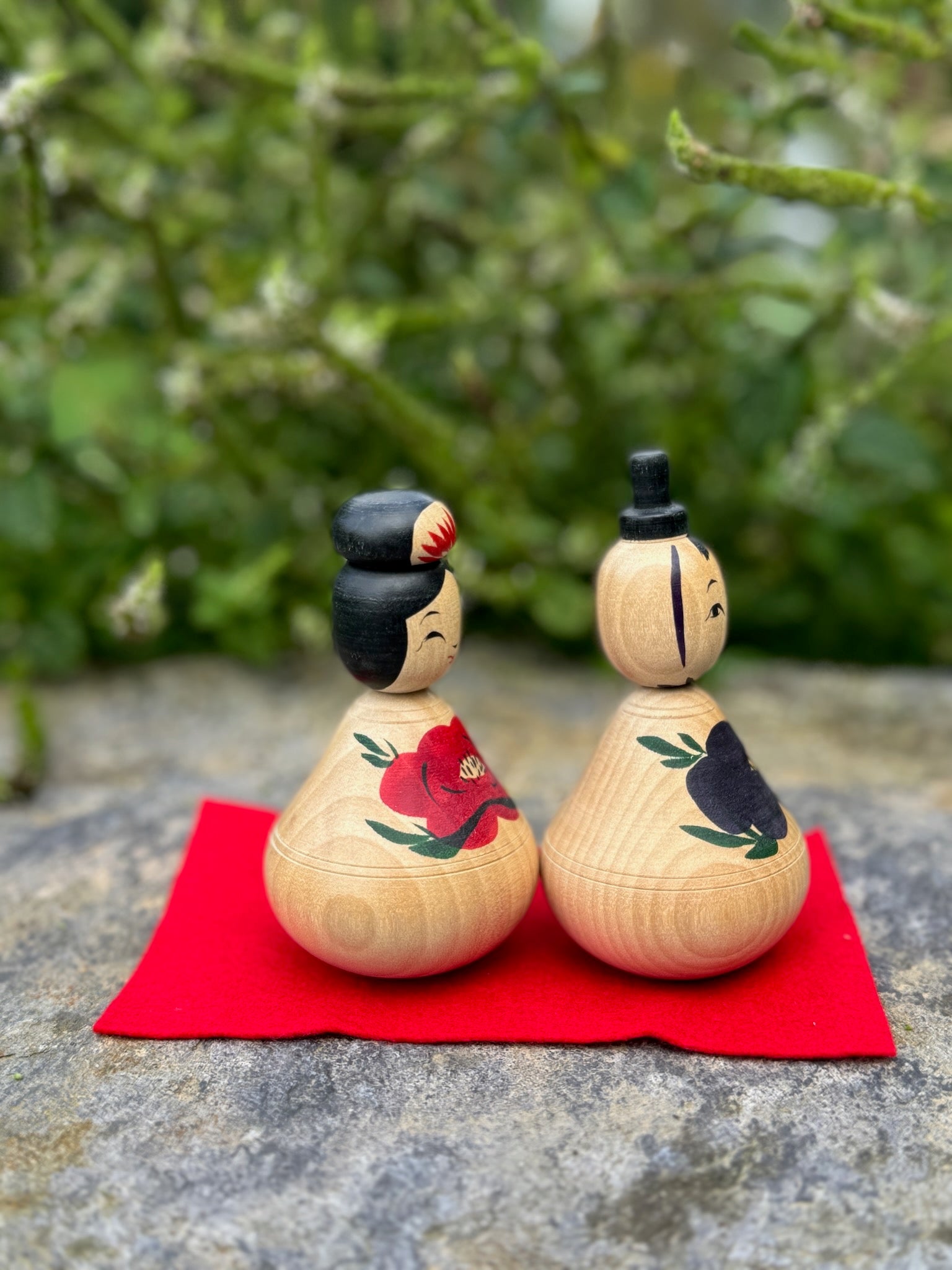 Couple de poupées kokeshi en bois avec motifs de pivoines rouges et bleues sur fond rouge vue profil 2