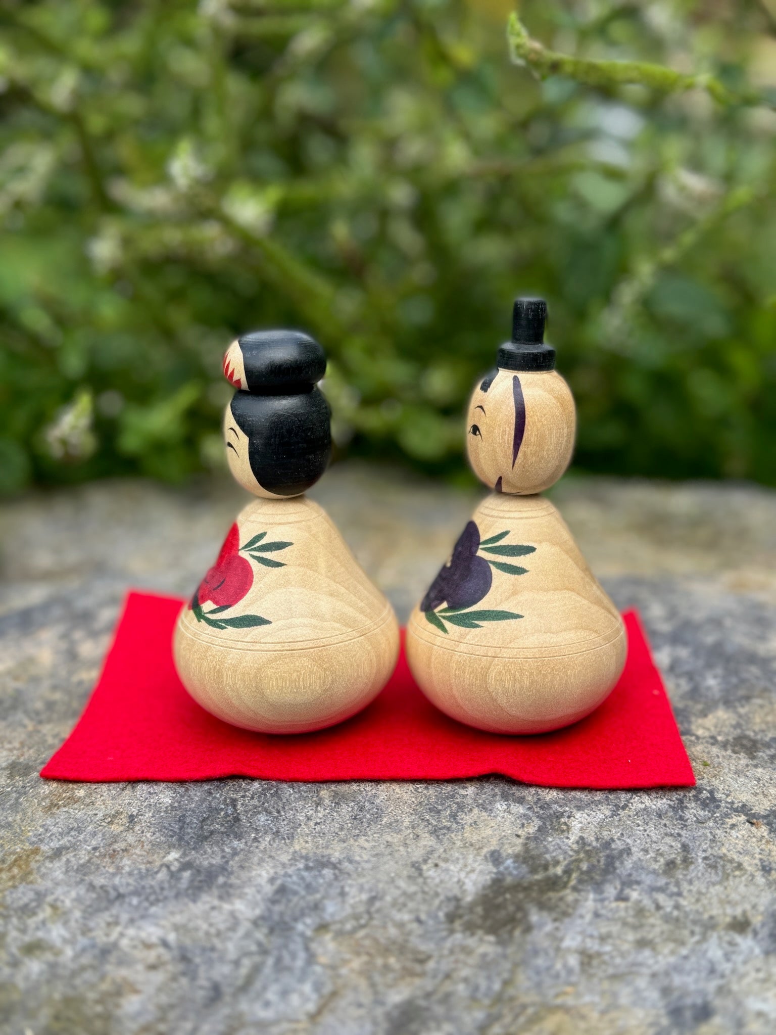 Couple de poupées kokeshi en bois avec motifs de pivoines rouges et bleues sur fond rouge vue profil 1