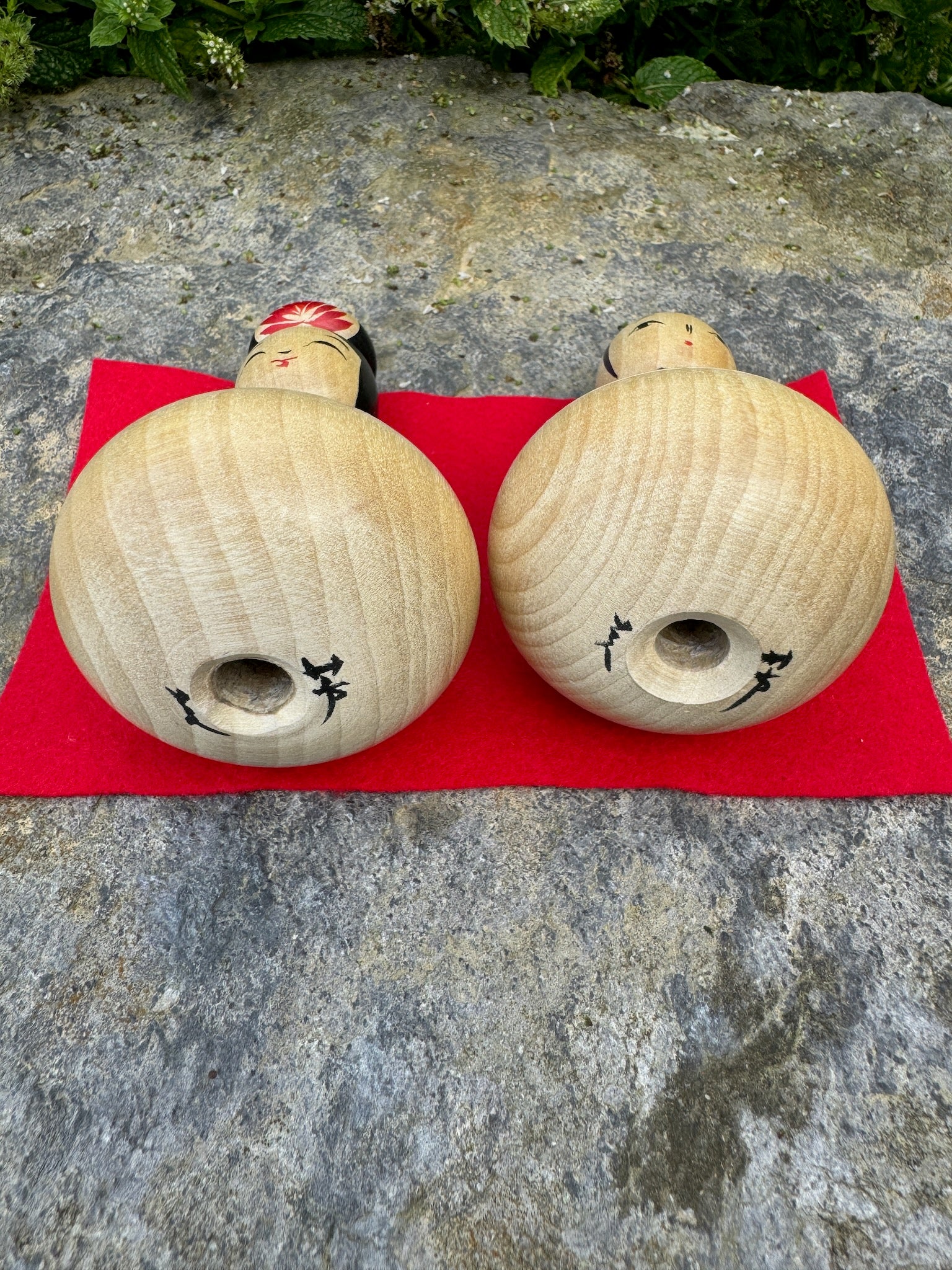 Couple de poupées kokeshi en bois avec motifs de pivoines rouges et bleues sur fond rouge vue dessous