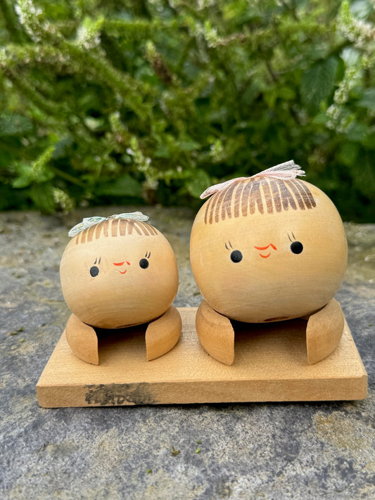 Couple de poupées kokeshi en bois sur socle, avec rubans rose et vert