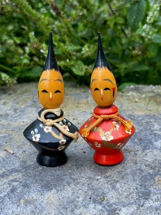 Couple de poupées kokeshi en bois, modèle pinceau habillées de kimonos rouge et noir avec des motifs floraux et coiffées d'une pointe de pinceau
