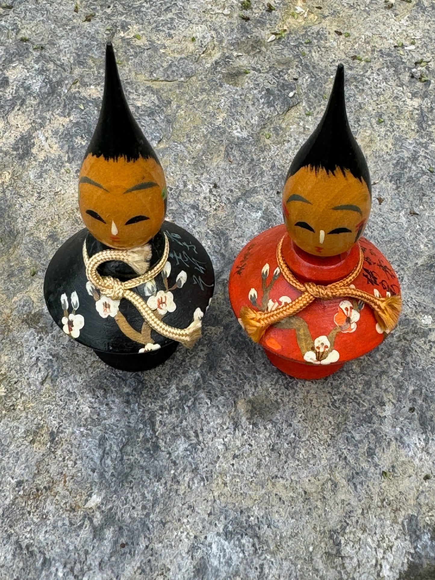 Couple de poupées kokeshi en bois, modèle pinceau habillées de kimonos rouge et noir avec des motifs floraux et coiffées d'une pointe de pinceau vue dessus