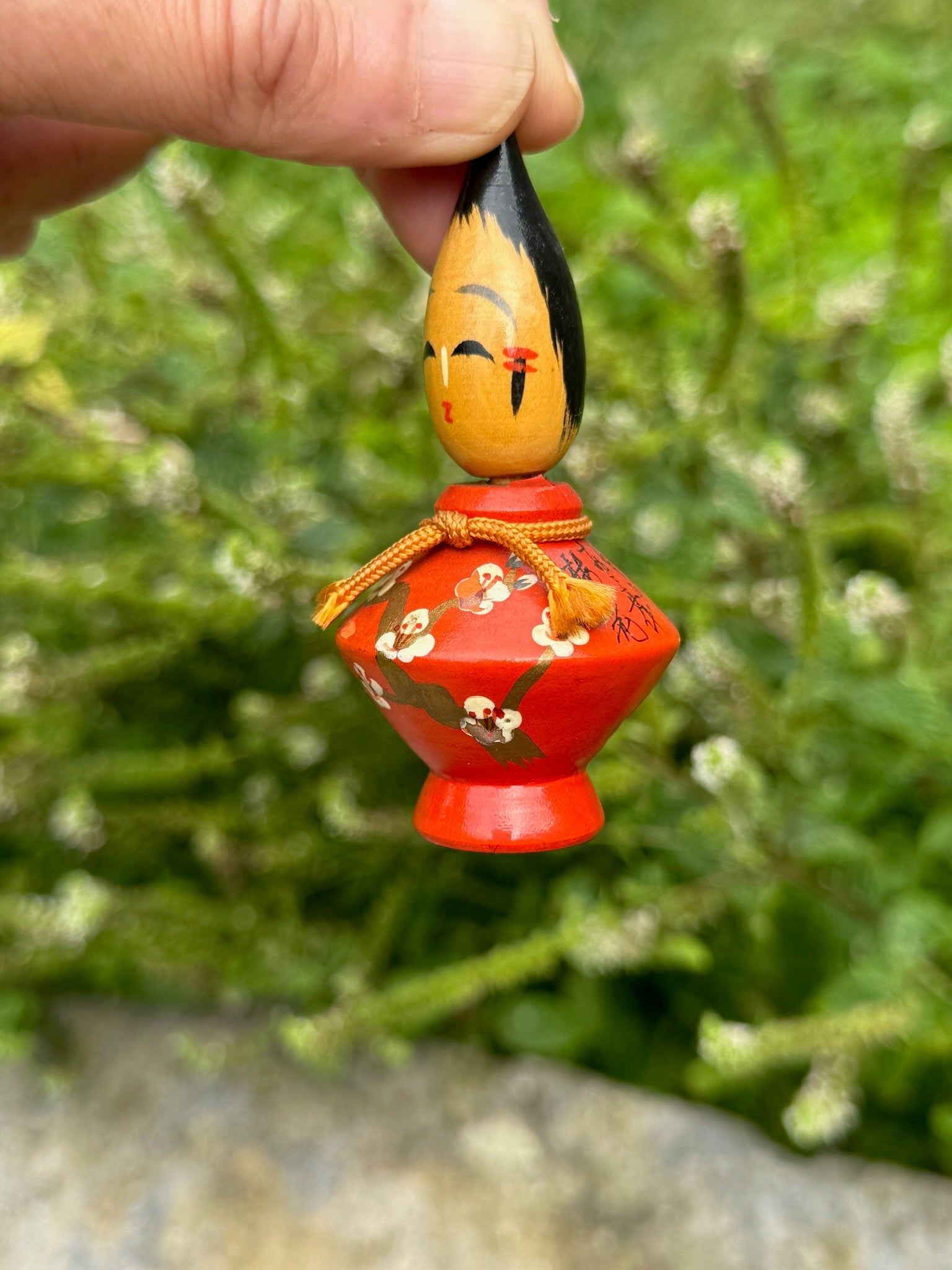 Couple de poupées kokeshi en bois, modèle pinceau habillées de kimonos rouge et noir avec des motifs floraux et coiffées d'une pointe de pinceau kokeshi rouge
