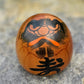 Poupée daruma en bois de forme ronde avec des détails peints noirs et rouges et un caractère japonais sur le devant.