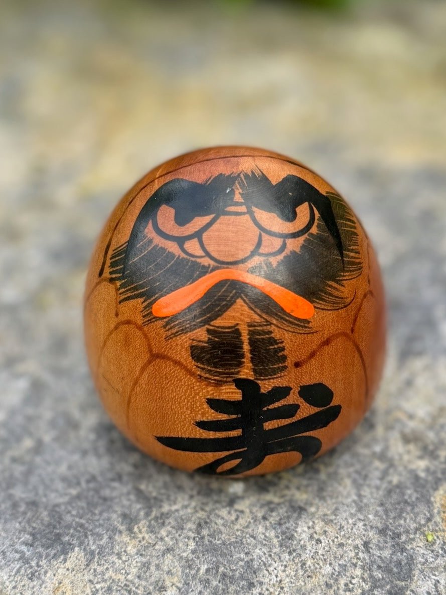 Poupée daruma en bois de forme ronde avec des détails peints noirs et rouges et un caractère japonais sur le devant.