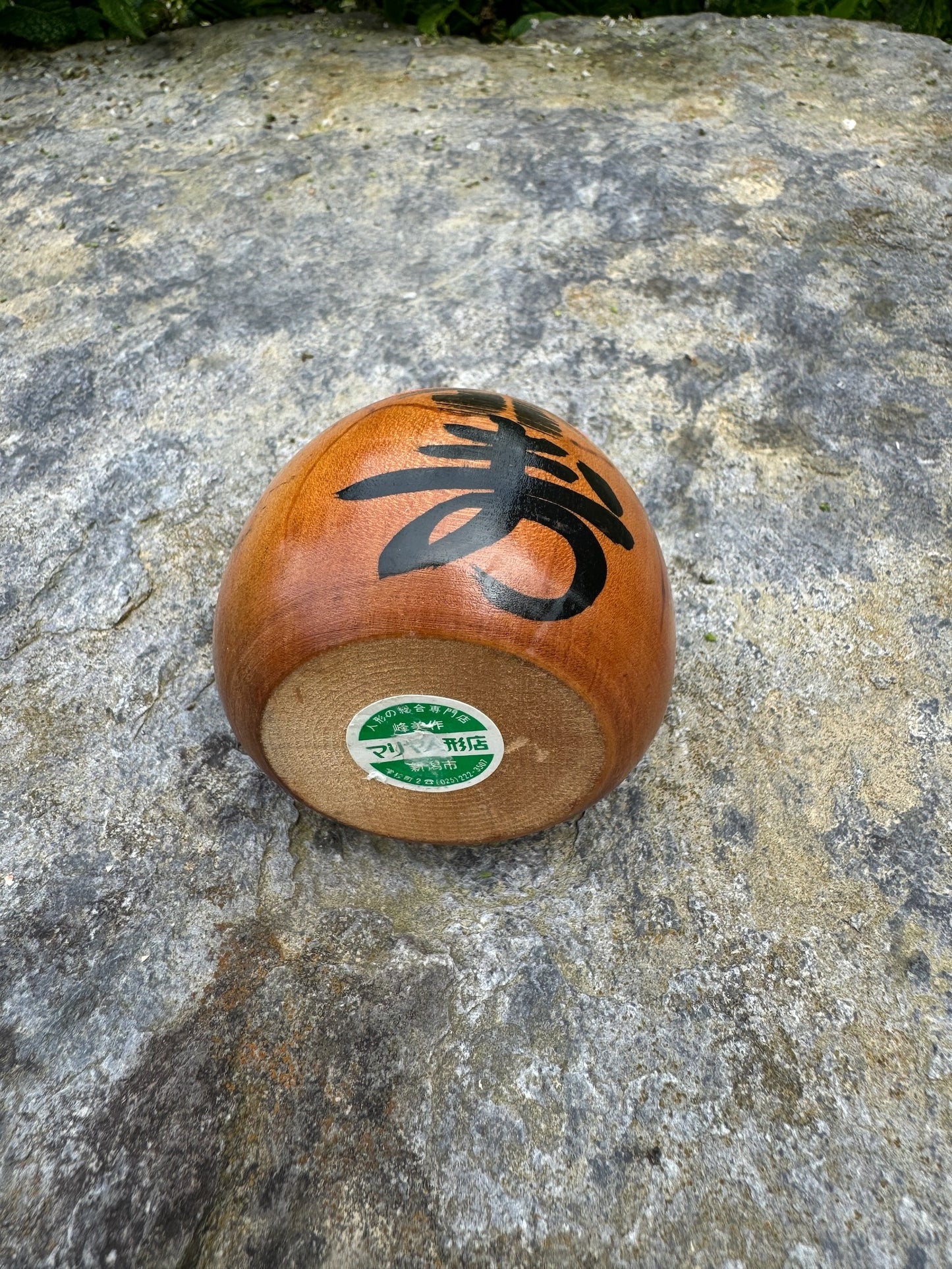 Poupée daruma en bois de forme ronde avec des détails peints noirs et rouges et un caractère japonais sur le devant vue dessous