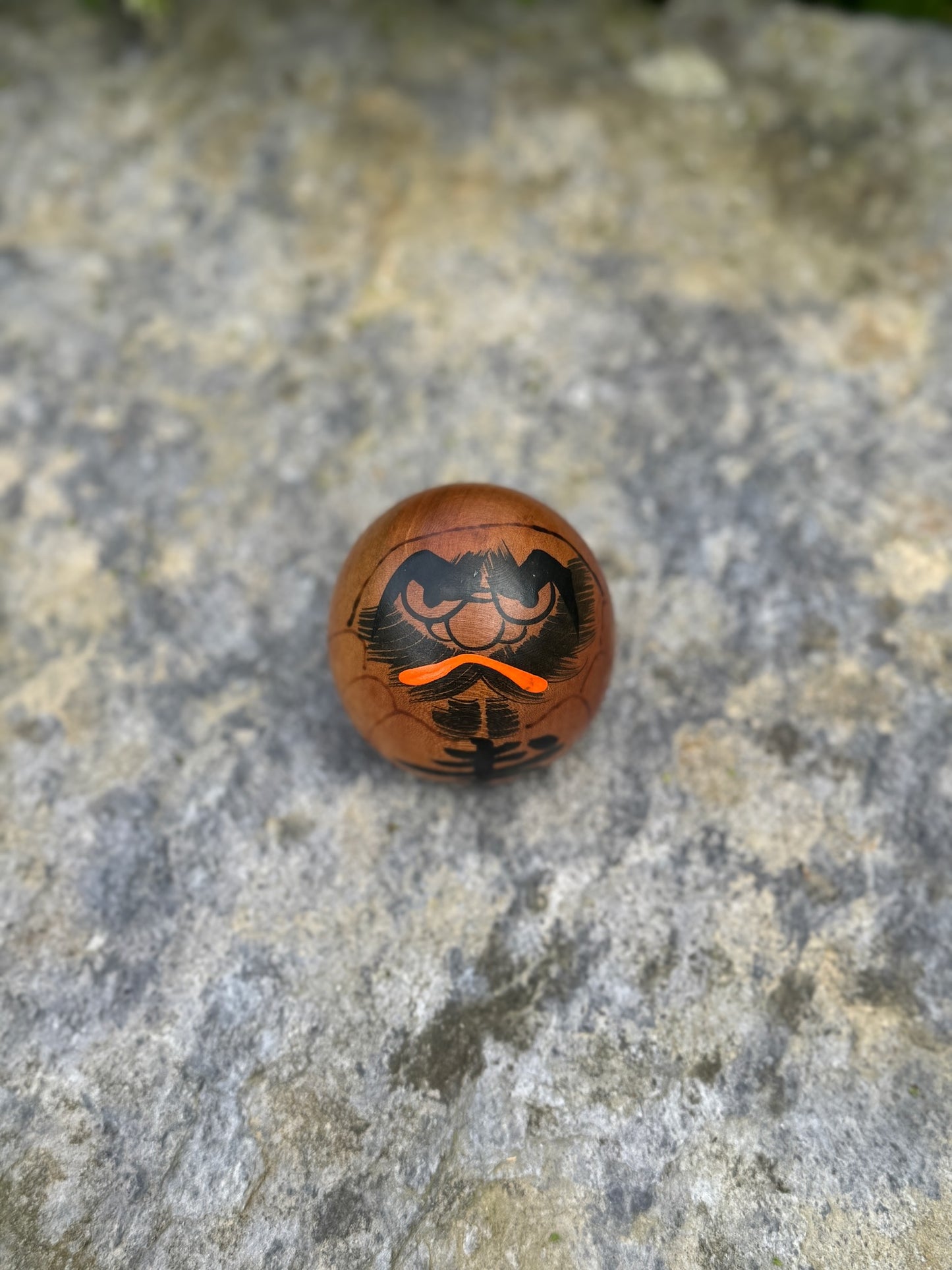 Poupée daruma en bois de forme ronde avec des détails peints noirs et rouges et un caractère japonais sur le devant vue dessus