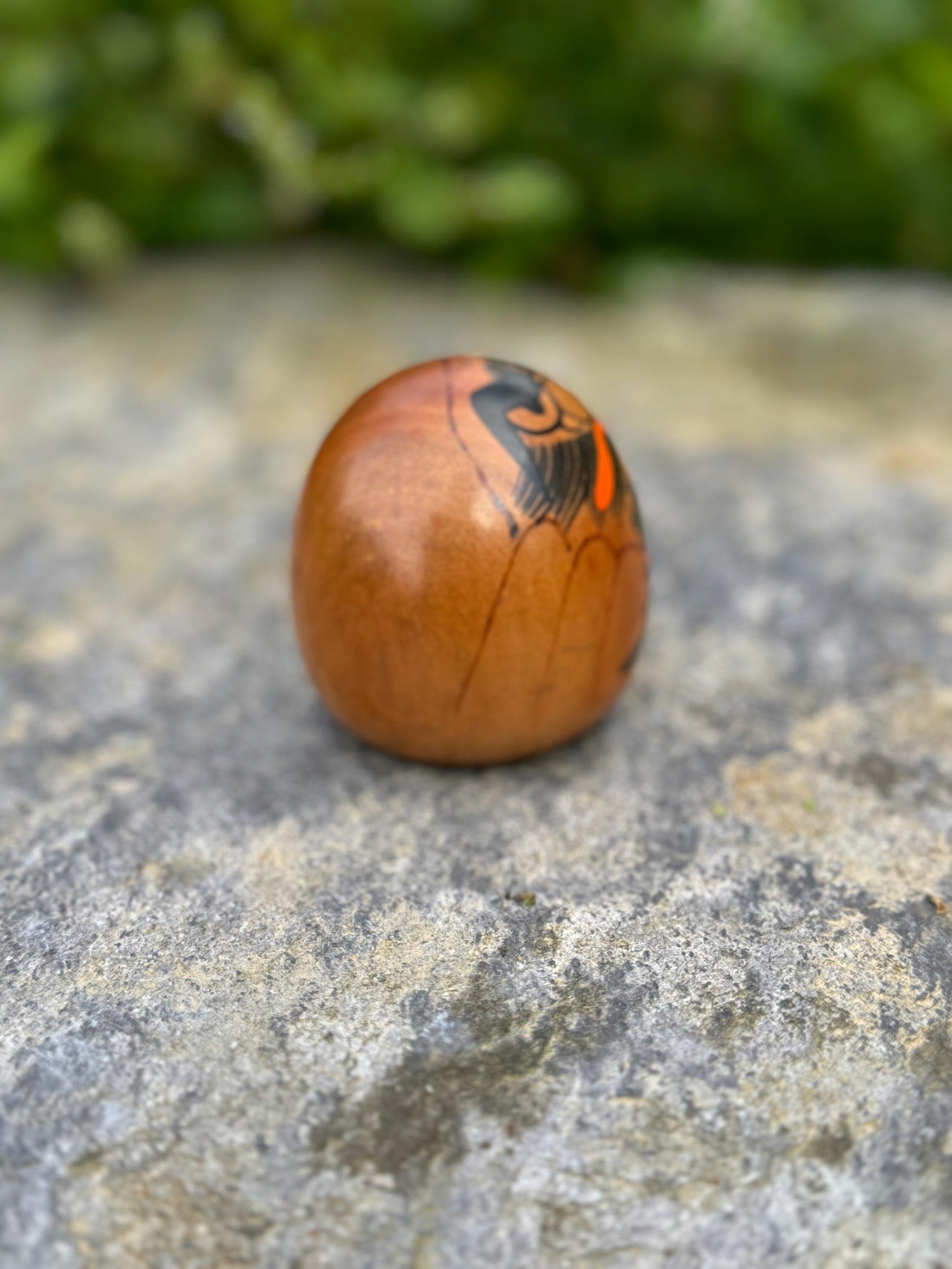 Poupée daruma en bois de forme ronde avec des détails peints noirs et rouges et un caractère japonais sur le devant vue de profil