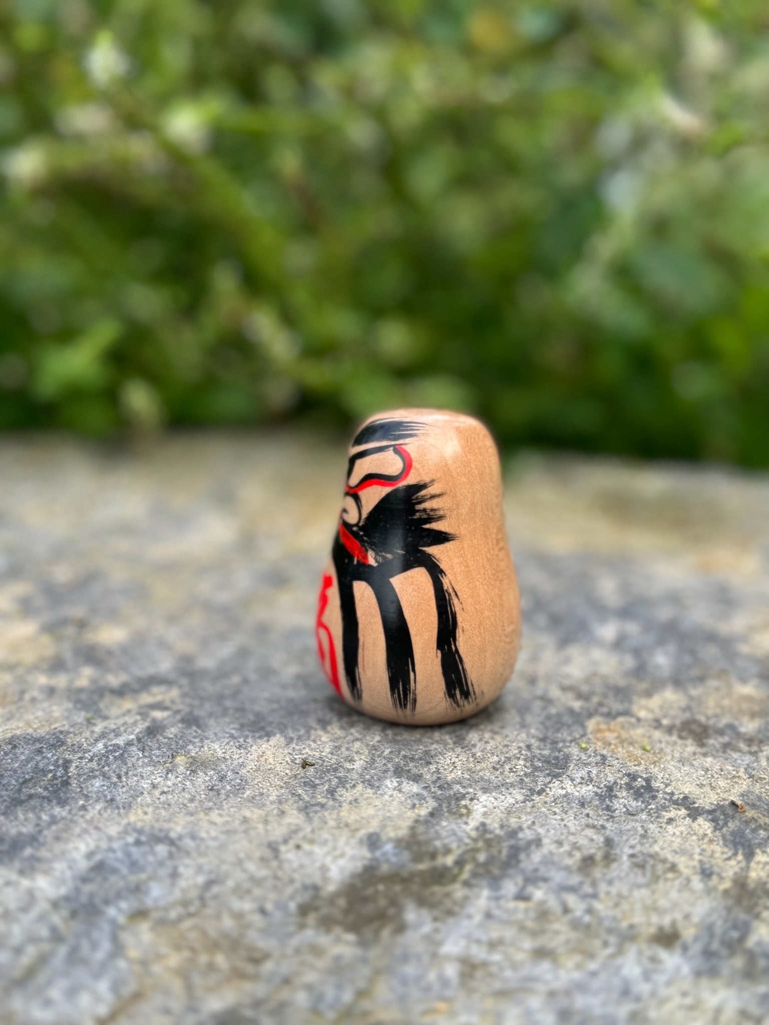 Daruma en bois blanc peint noir et rouge avec calligraphie profil gauche