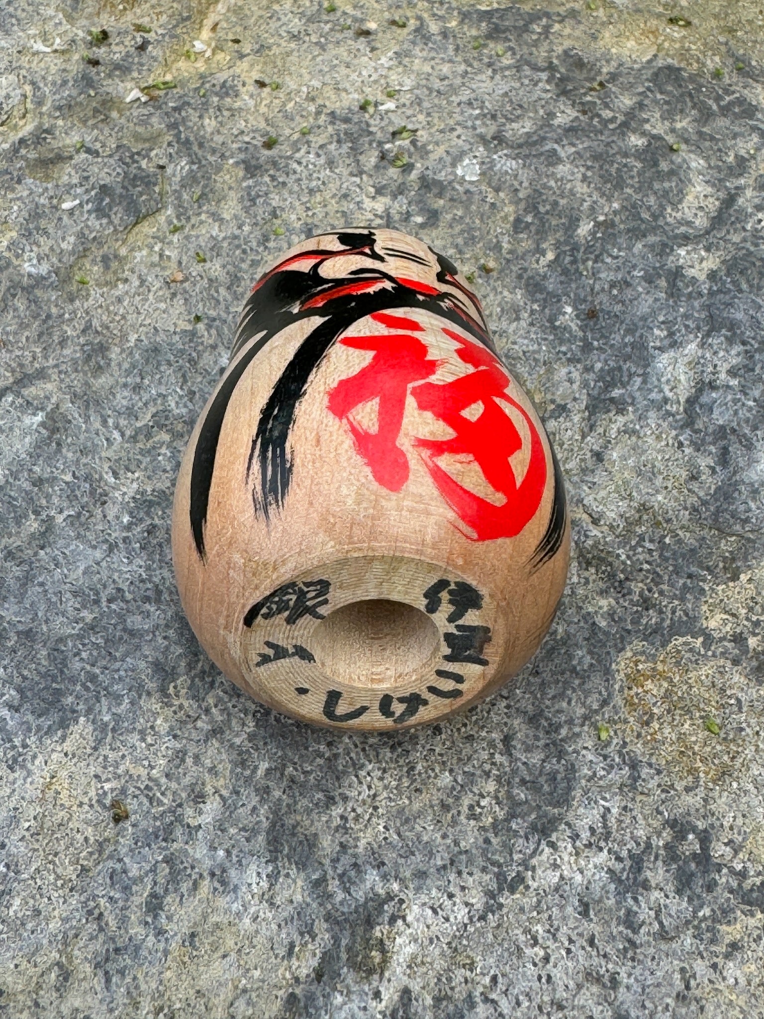 Daruma en bois blanc peint noir et rouge avec calligraphie vue dessous