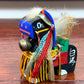 mini cheval japonais en bois chagu chagu, noir avec décorations de couleurs vives et clochette, profil gauche avec calligraphie sur flanc