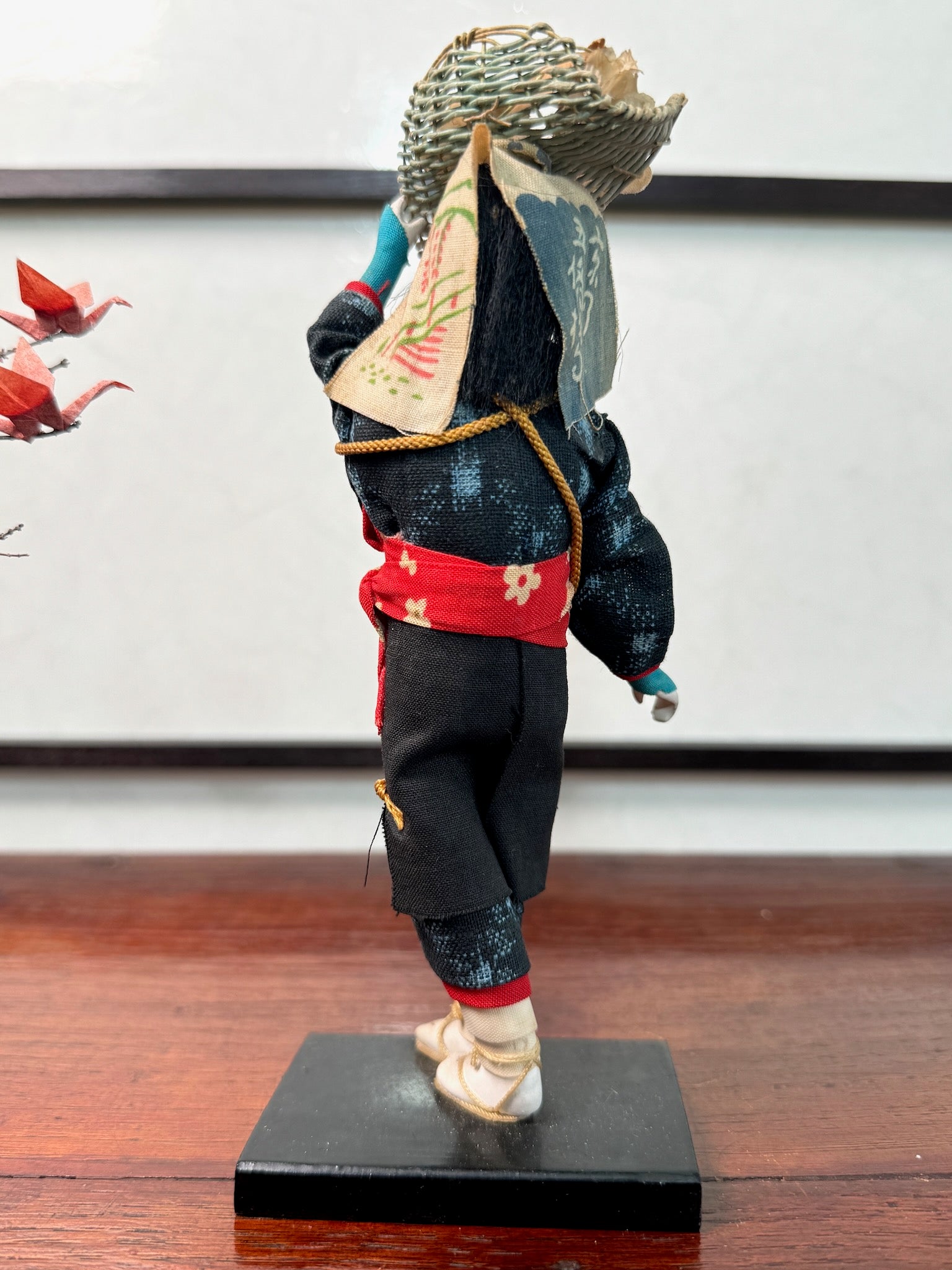 poupée japonaise marchande de fleurs avec panier sur la tête, en kimono bleu et obi rouge, vu de dos