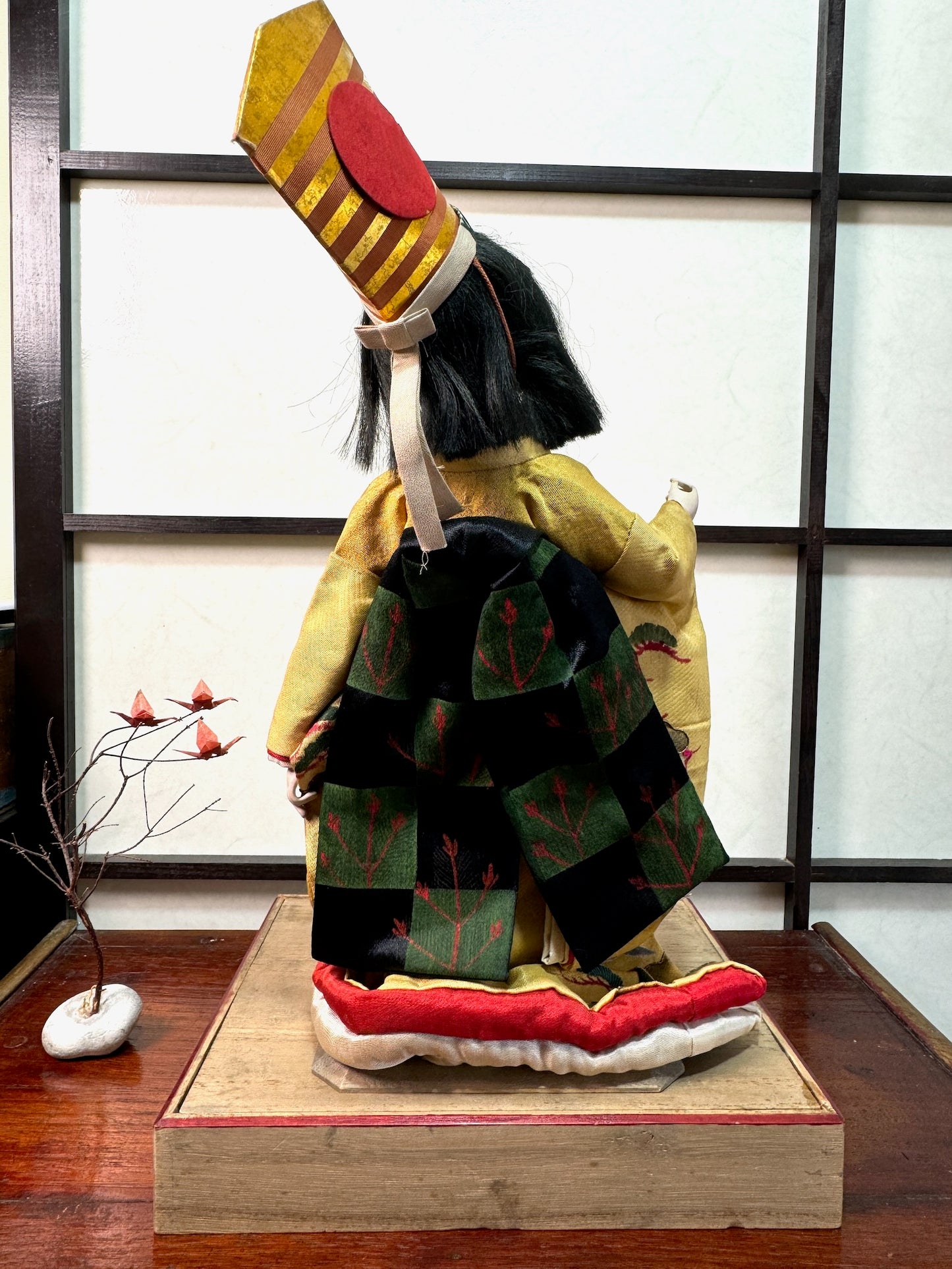 poupée japonaise ancienne en kimono jaune à motif de grues et massif de pin, vu de dos, son obi noir et vert noué en gros noeud