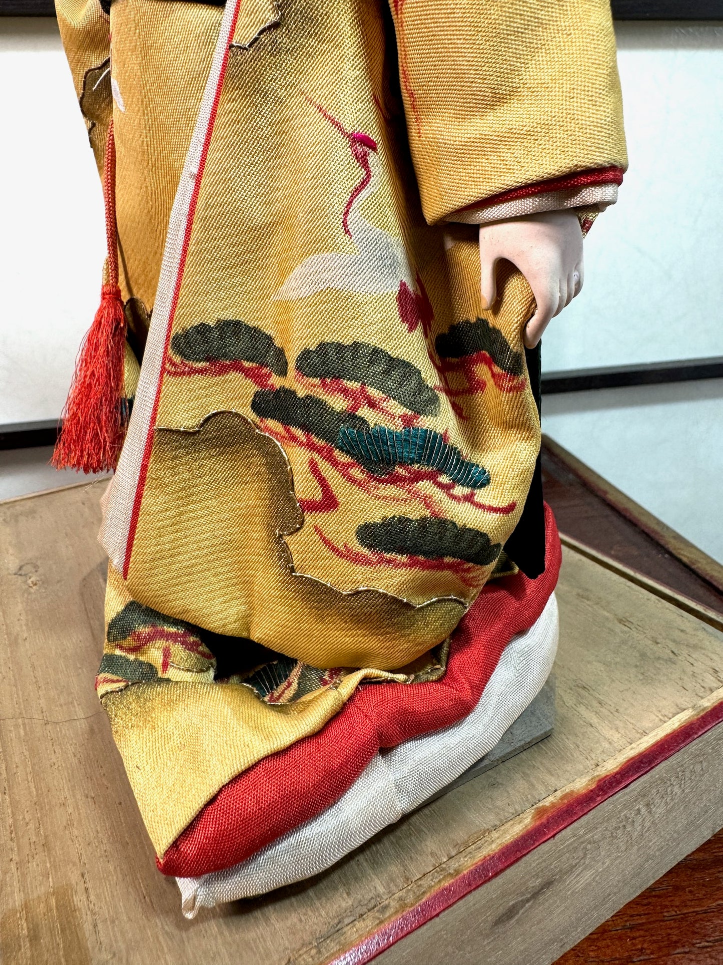 poupée japonaise ancienne en kimono jaune à motif de grues et massif de pin, gros plan sur les pins