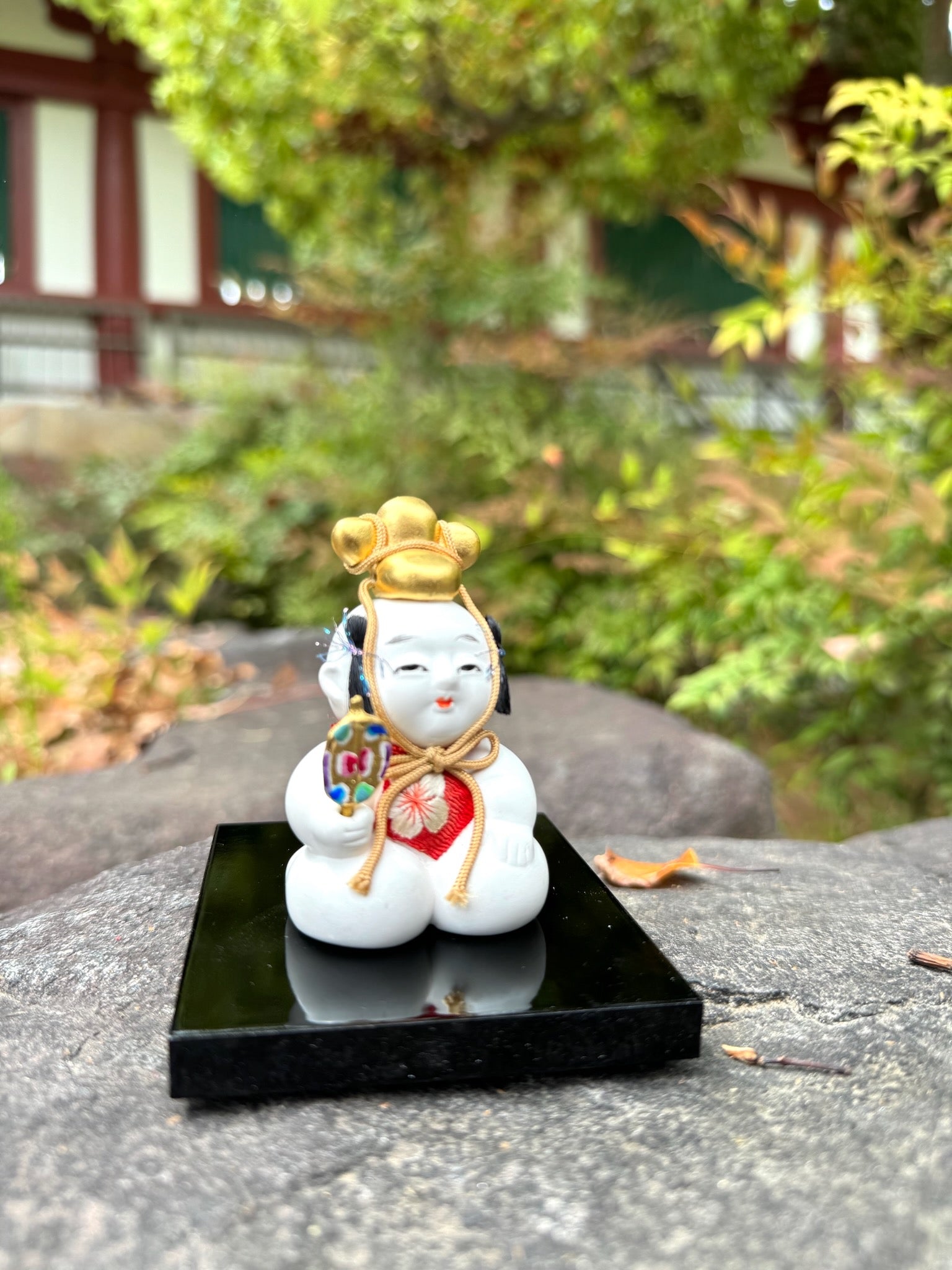 Poupée japonaise traditionnelle gosho, petit garçon potelé, tient éventail dans sa main et chapeau doré sur sa tête. Sur socle noir laqué.