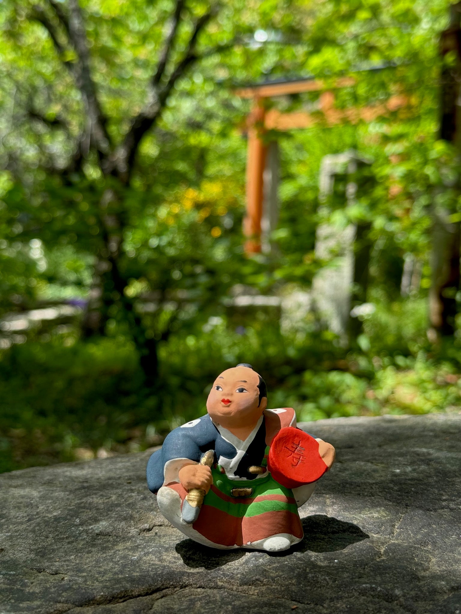 Poupée Samourai en porcelaine biscuit d'Hakata, coupe de sake rouge sous le bras et dague, kimono bleu et hakama vert et marron. Peint à la main.